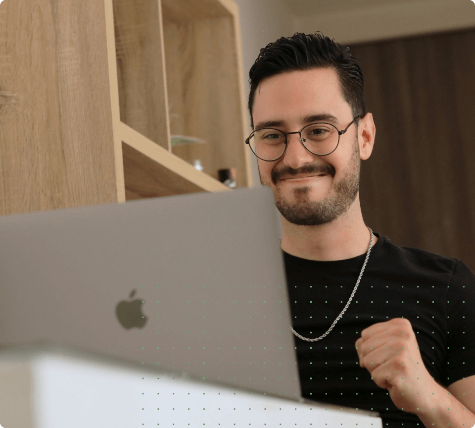 Man smiling and clenching his fist in excitement while looking at a laptop.